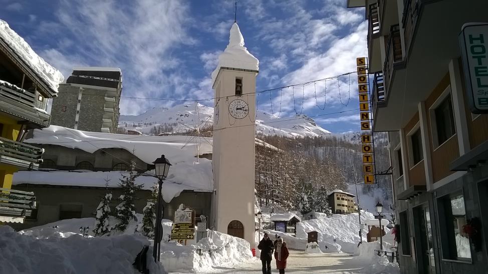 Charming Cervinia town center. Small church with a bell tower, tons of snow and mountains behind