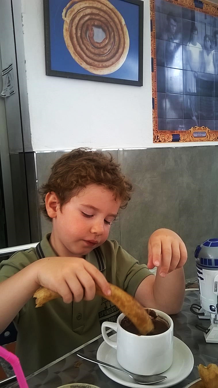 My son is tasting churros, while dipping it into a hot chocolate Marbella
