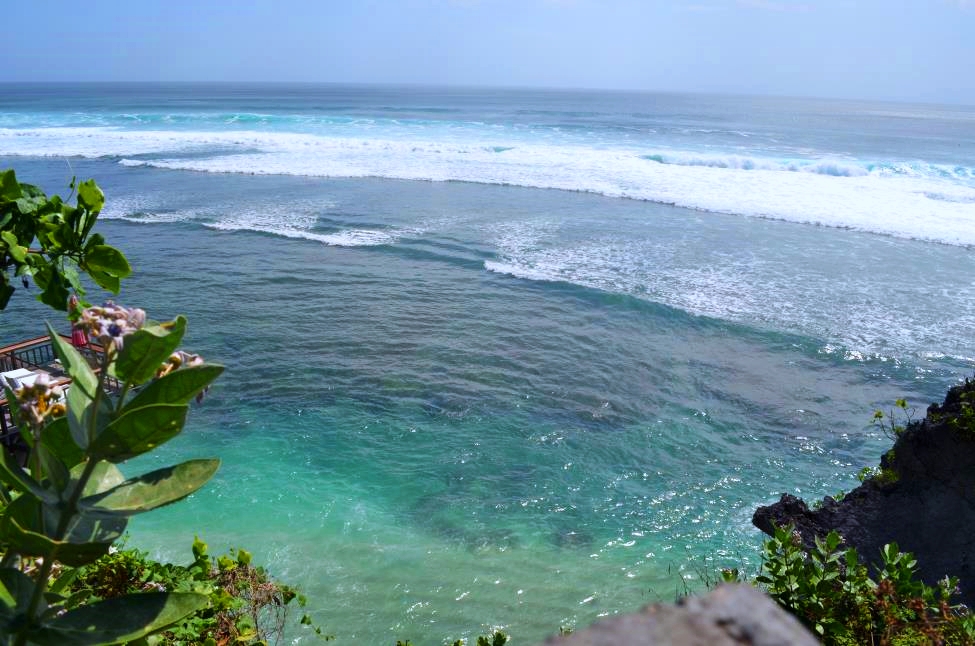 Surfing paradise of Uluwatu. View from the terrace on the top of the town with flowers, rocks and blue ocean intersected by the waves