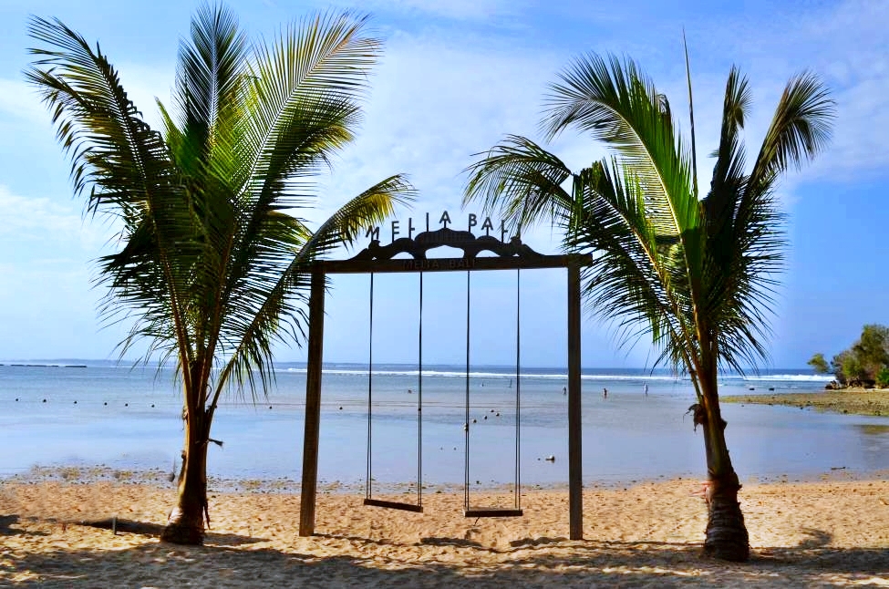 Postcard view during afternoon stroll, Nusa Dua, Bali. Two swings are between two palm trees with ocean in the background