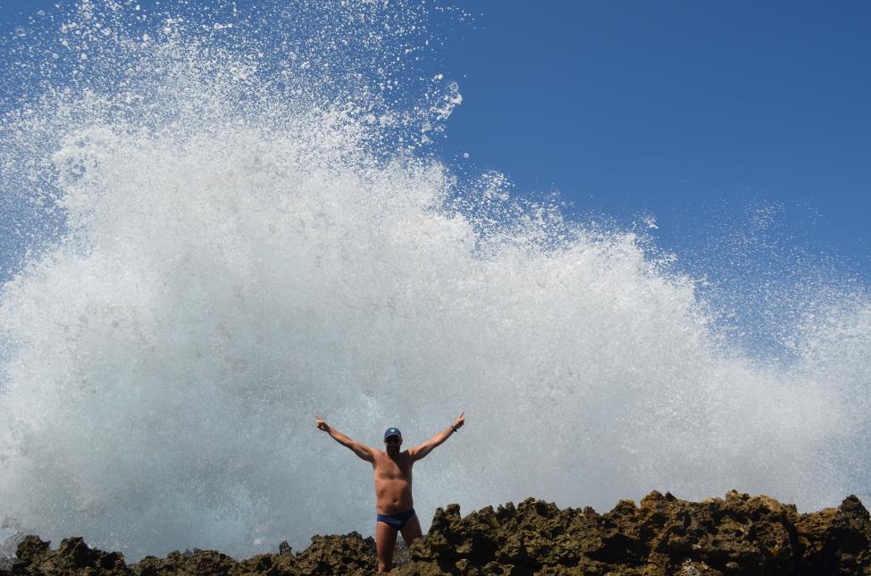 My son is challenging giant ocean wave which crushes into the rocky cliff