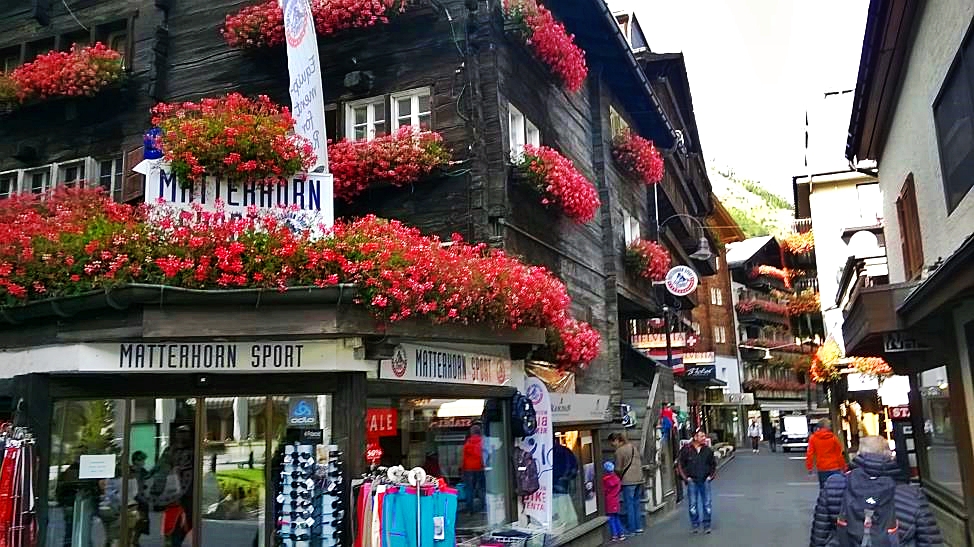 Main street in Zermatt - Bahnhofstrasse with flowers on the balconies, shops and tourists