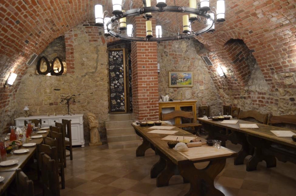 Mediavla setting for pierogi cooking class with lomg wooden tables, brick vaults and a chandelier