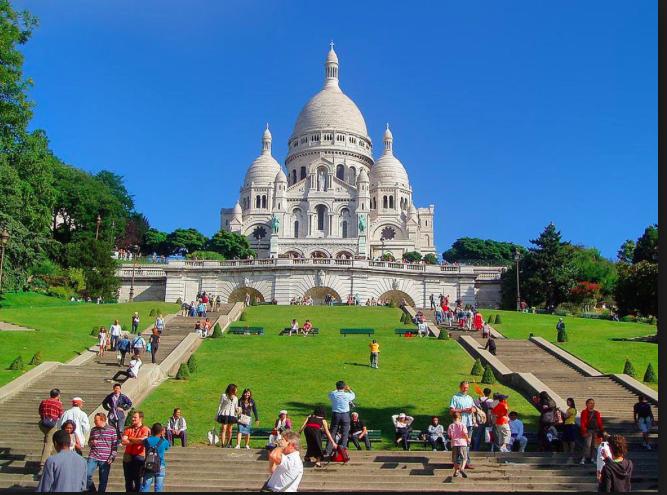 postcard view of shining white Sacre Coeur Basilica with side flights of steps and blue sky background
